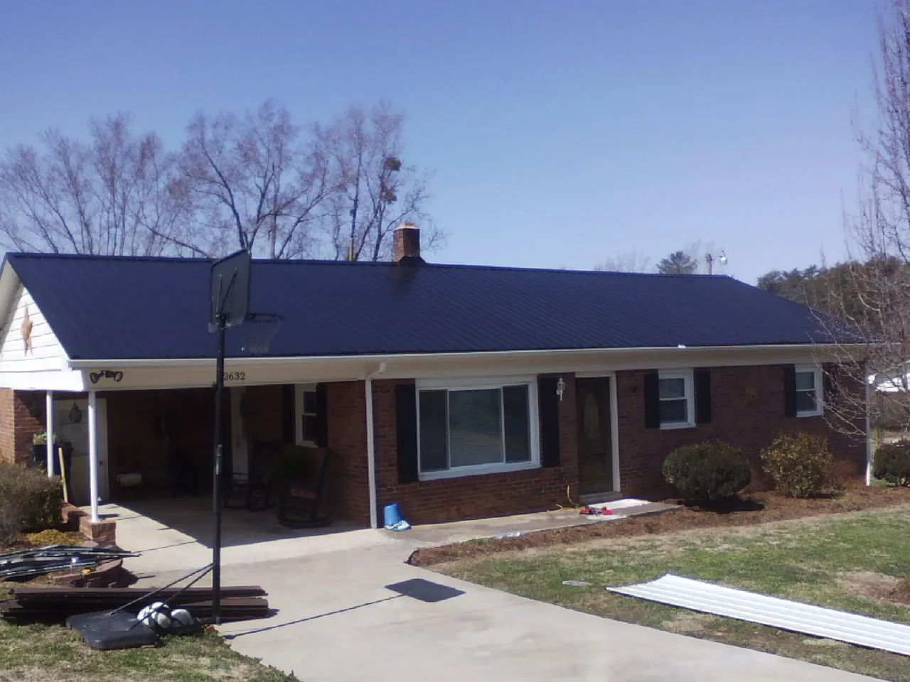 Finished dark blue metal roof on a brick ranch with a carport in Ada